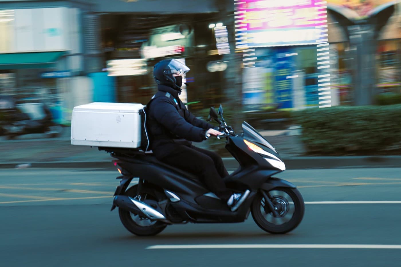 Un coursier à scooter avec un coffre de livraison à l’arrière, dans une rue de la ville
